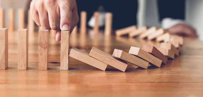 Dominos falling over and being stopped by a hand, representing crisis management